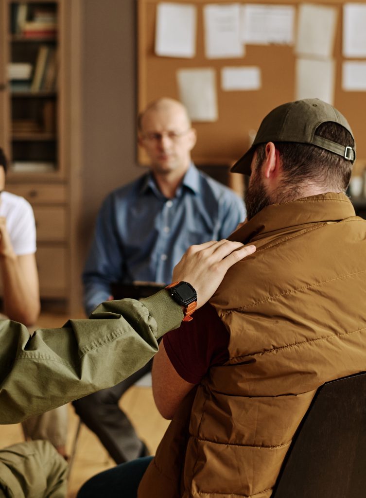 One of attendants of psychological session keeping hand on shoulder of upset man while comforting him and expressing empathy