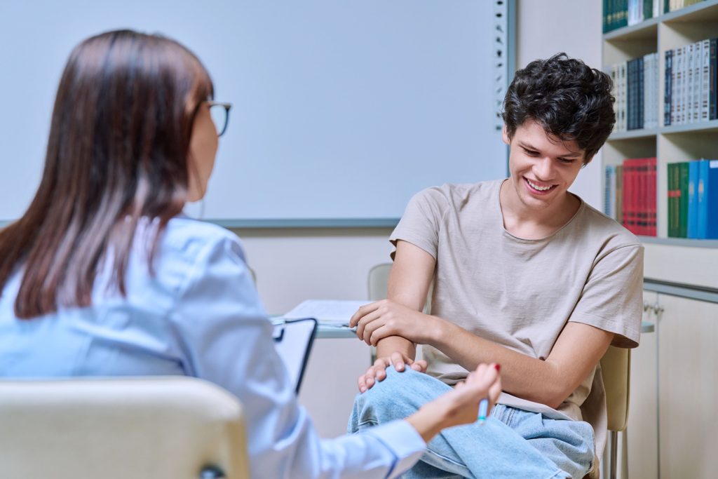 Young guy student 18-20 years old at meeting with psychologist, social worker, college counselor, talking in office. Psychology, psychotherapy, socialization, help support, mental health concept