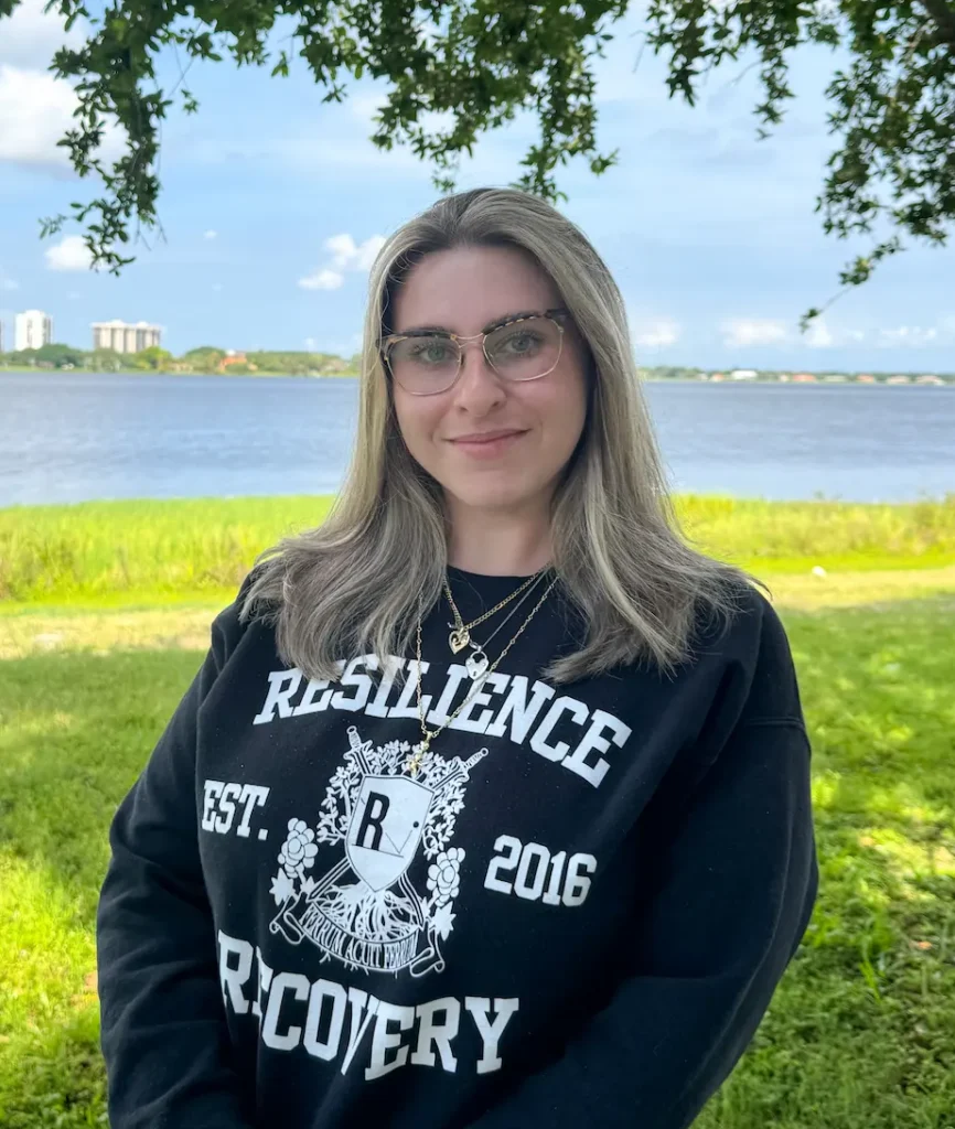 Case manager standing outdoors by a waterfront wearing a Resilience Recovery sweatshirt
