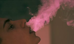 Teen boy smokes vape.